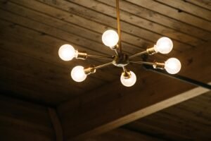 Modern brass chandelier with exposed bulbs hanging from a wooden ceiling, providing warm ambient lighting.