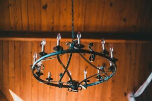 Rustic wrought iron chandelier with candle-shaped bulbs hanging from a wooden ceiling, creating a vintage farmhouse ambiance.